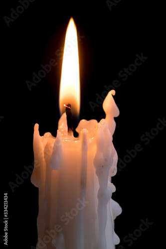 Candleflame on a lit candle. White candle burning, isolated on a dark background