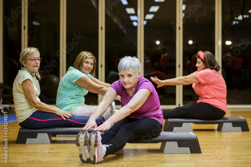 Gruppo di anziane signore si allenano in palestra facendo stretching sugli step photo