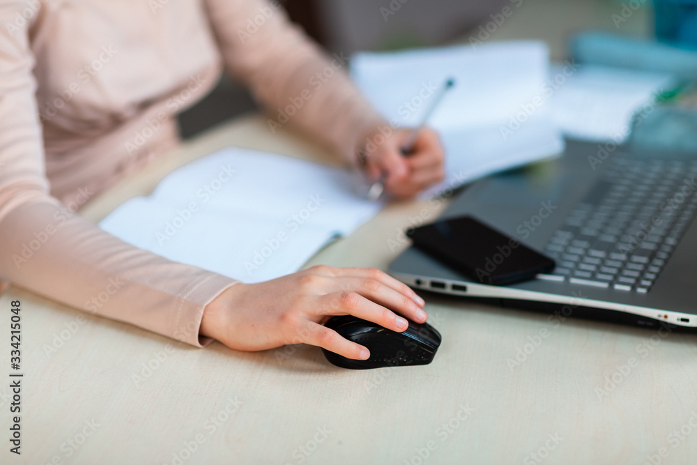 Close up of young school girl left-handed working at home in her room with a laptop and class notes studying in a virtual class. Distance education and learning concept during quarantine Close up of young school girl left-handed working at home in her room with a laptop and class notes studying in a virtual class. Distance education and learning concept during quarantine