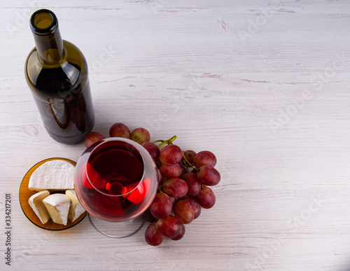 Hi angle horizontal perspective with a one traditional round glass filled with dark red wine and red grape and bootle with white cheese and a thin leg on a wooden table with copy space for your text