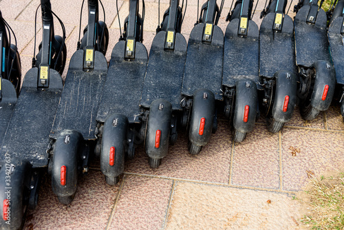 Several black electric scooters parked in a row, for rent.