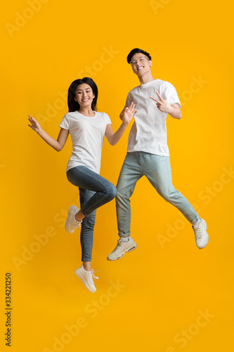 Excited asian couple of hipsters having fun over yellow