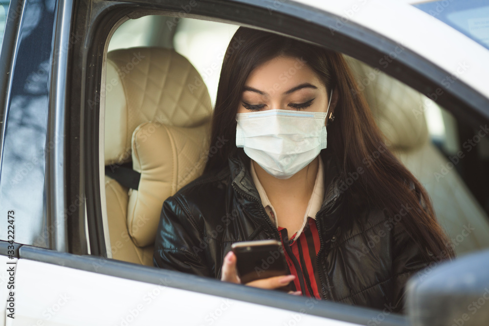 beautiful young woman in medical face mask in a car with a phone in her hand
