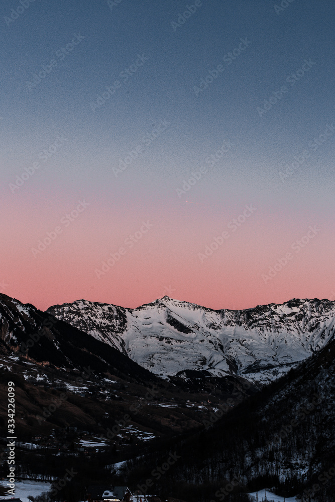 A beautiful sunset sky with shades of fading pink and blue over a snowy mountain in winter