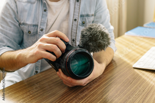 A photographer or videographer holding his camera. The camera has an external microphone for vlogs and videos on social networks. Telecommuting