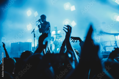 Concert crowd attending a concert, people silhouettes are visible, backlit by stage lights, raised hands. © Alfredo