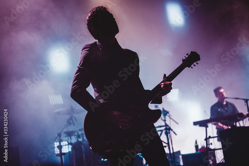 Silhouette of a man playing the guitar on stage. Dark background, smoke, spotlights