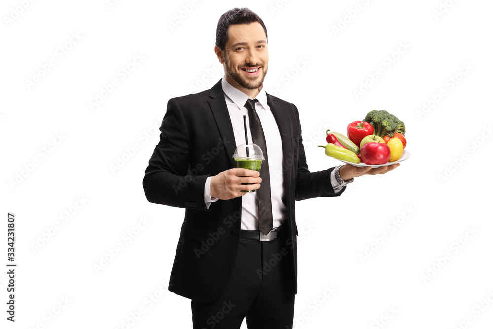 Young formal man in a suit holding a smoothie and a pile od healthy vegetables and fruits Young formal man in a suit holding a smoothie and a pile od healthy vegetables and fruits