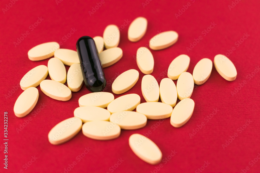 A lot of white pills and one black capsule on a red background. A lot of white pills and one black capsule on a red background.
