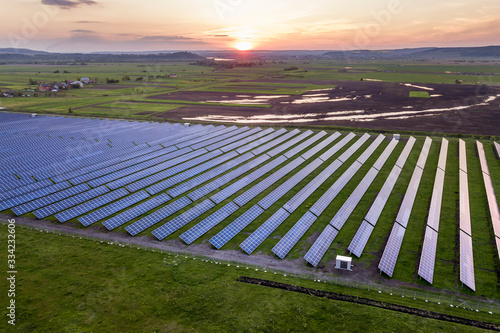 Blue solar photo voltaic panels system producing renewable clean energy on rural landscape and setting sun background.