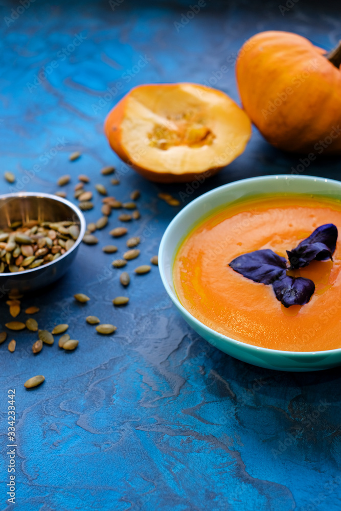 Pumpkin soup with purple Basil on a blue background with crispy toasted pumpkin seeds. Pumpkin soup with purple Basil on a blue background with crispy toasted pumpkin seeds.