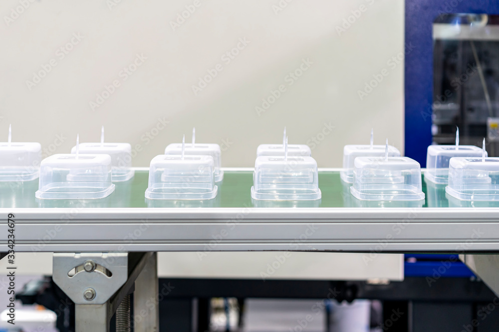 Many row of clear plastic cup or box after made by plastic injection mold machine on automatic conveyor belt during manufacturing process in factory Many row of clear plastic cup or box after made by plastic injection mold machine on automatic conveyor belt during manufacturing process in factory