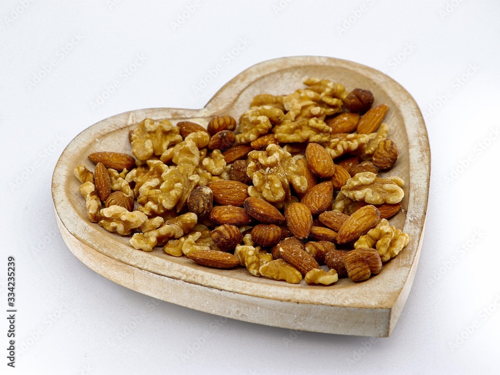 Mix of different nuts on the plate: almond, hazelnut, walnut in a heart form on the white background Mix of different nuts on the plate: almond, hazelnut, walnut in a heart form on the white background