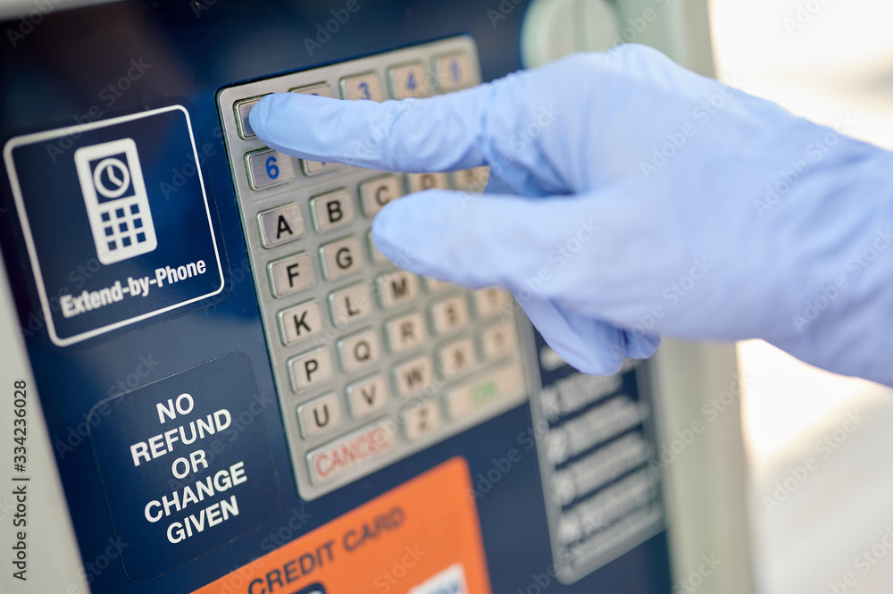 The right hand in the blue glove on the dial on the parking meter The right hand in the blue glove on the dial on the parking meter