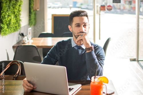 Φωτογραφία Portrait of handsome young man in smart casual clothing working on laptop in caf