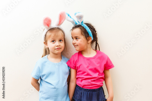Two smiling girls with rabbit ears holding a box with easter eggs on background.