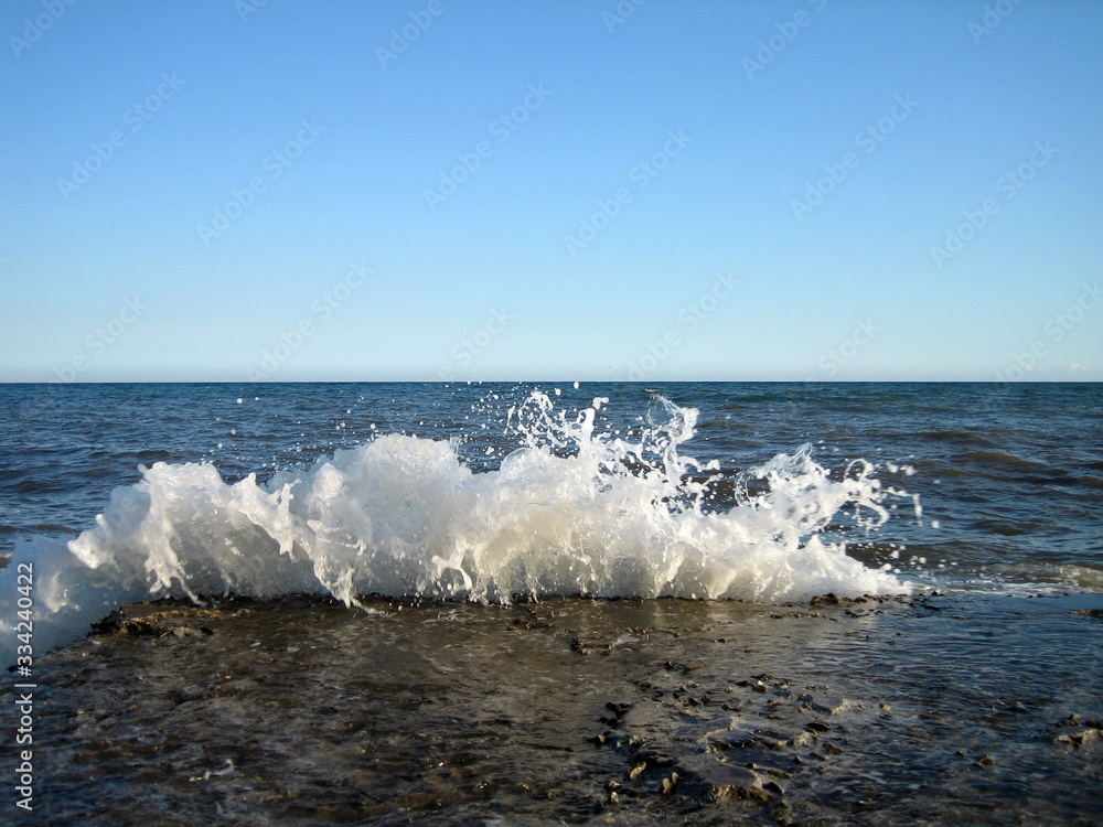 Fototapeta premium A splash of sea water on a stone pier with lots of foam and spray on a Sunny day against a flat horizon.