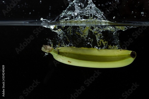 Close up view of colorful banana falling in water on black background. Gorgeous backgrounds.