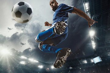Professional football or soccer player in action on stadium with flashlights, kicking ball for winning goal, wide angle. Concept of sport, competition, motion, overcoming. Field presence effect.