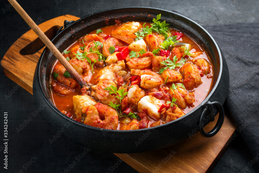 Traditional American fish stew cioppino with prawns, and fish as closeup in a modern design cast-iron roasting dish