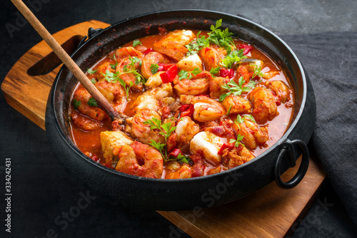 Traditional American fish stew cioppino with prawns, and fish as closeup in a modern design cast-iron roasting dish