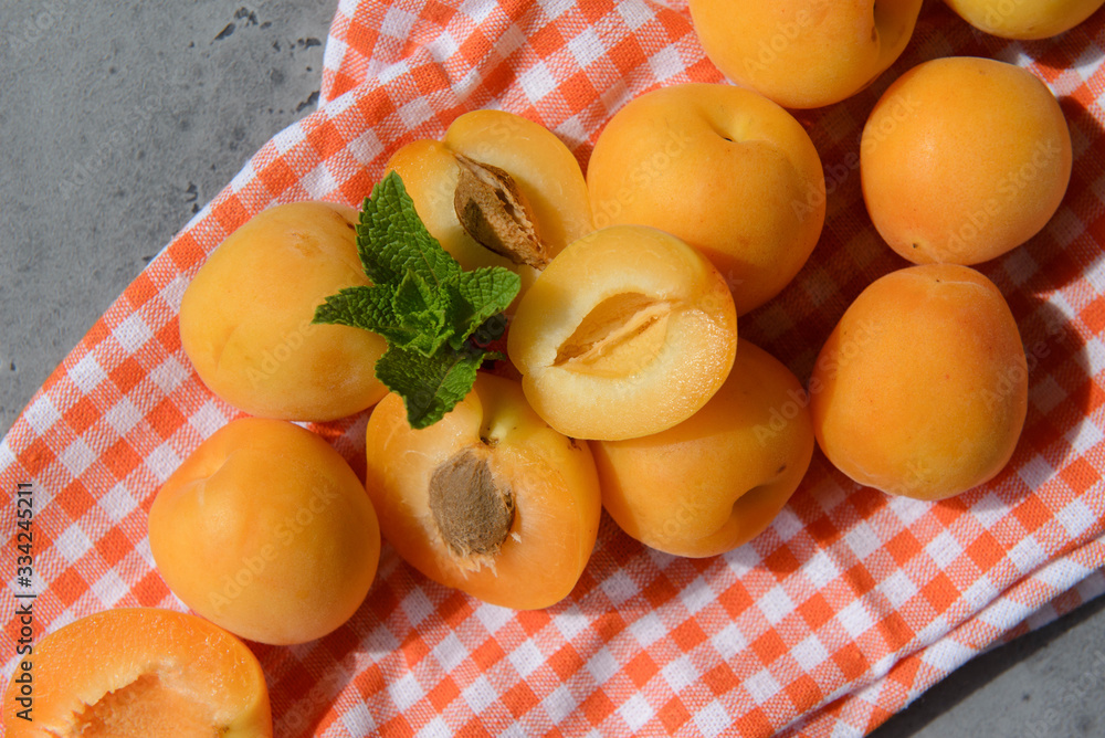 fresh juicy apricots, a sprig of mint on an orange towel, gray background fresh juicy apricots, a sprig of mint on an orange towel, gray background