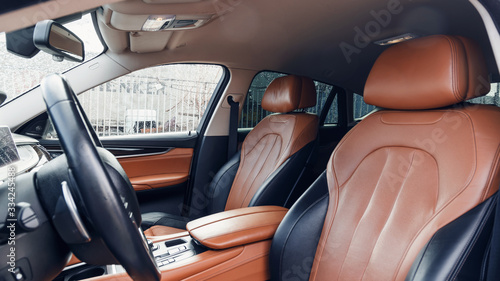 Black and brown leather car interior. Modern car illuminated dashboard. Luxurious car instrument cluster. Close up shot of automobile instrument panel. Modern car interior dashboard and steering wheel