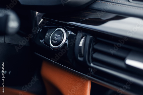 Car Start-Stop Engine Button of a modern car in the interior of the expensive car. Black and brown leather car interior. Illuminated dashboard. Luxurious car instrument cluster. Close up © svetlichniy_igor