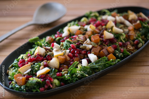 Winter salad with pomegranates, pears, kale sweet potato and pumpkin seeds served on a black serving plate in a beautiful setting