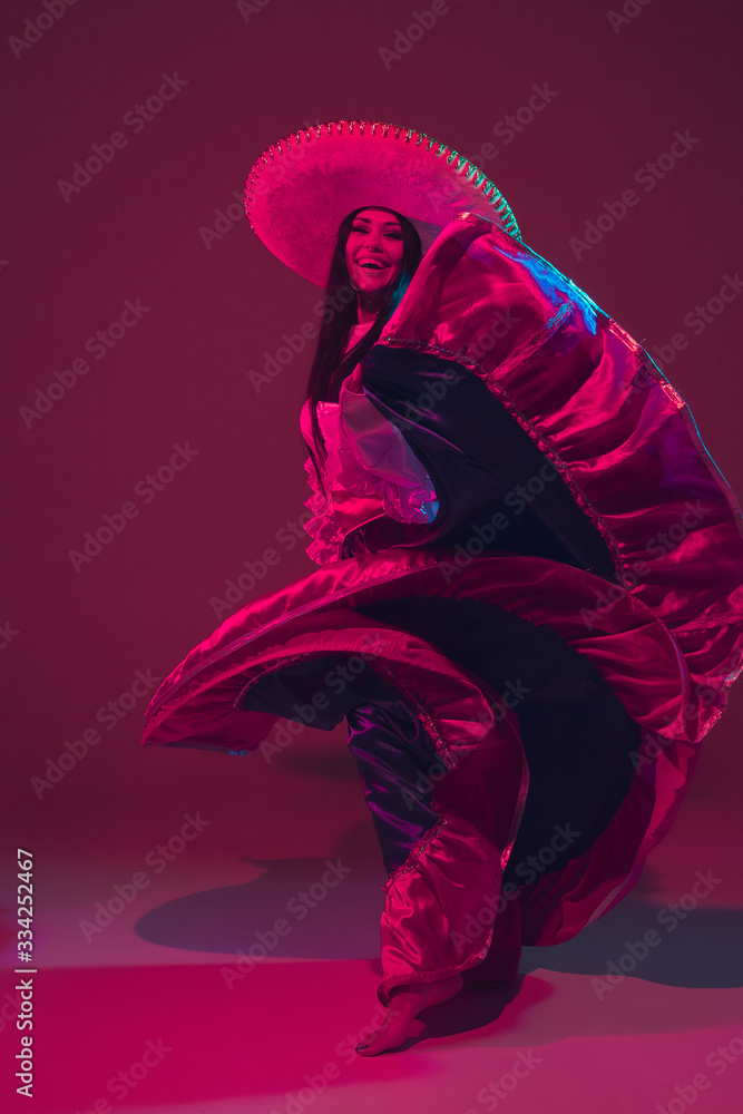 Fabulous Cinco de Mayo female dancer on purple studio background in neon light. Beautiful female model in traditional costume and sombrero dancing. Celebration, holiday, beauty and fashion concept.