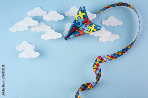 Autism awareness day or month. Paper plane in origami style with autism awareness puzzle ribbon on blue background.