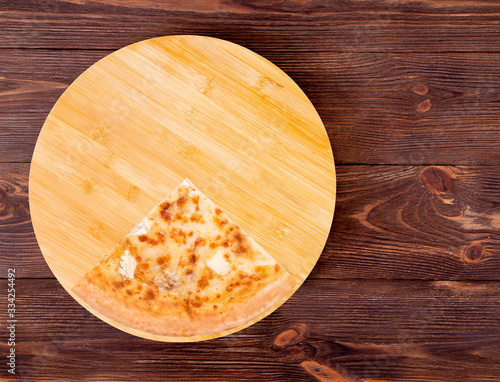 A slice of pizza five cheeses on bamboo bottom, on wooden table, top view, space for text