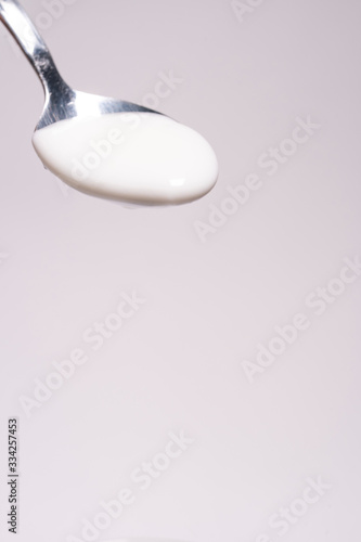 Homemade organic dairy product in a glass cup. Woman's hand raises a full spoon with yogurt on a white background