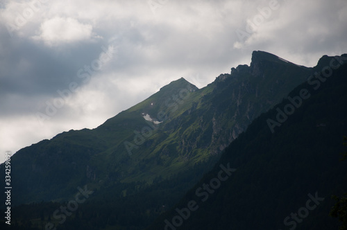 Dramatic view of mountains, with green grass and dark clouds, sun shining through the clouds.