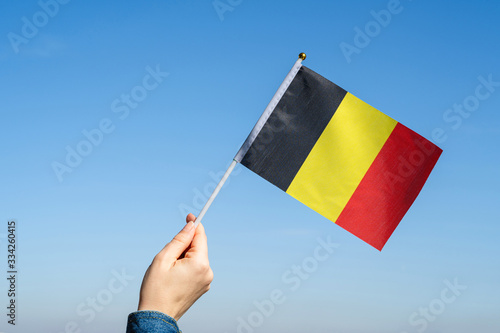 Fotografie Woman hand with Belgian swaying flag on the blue sky