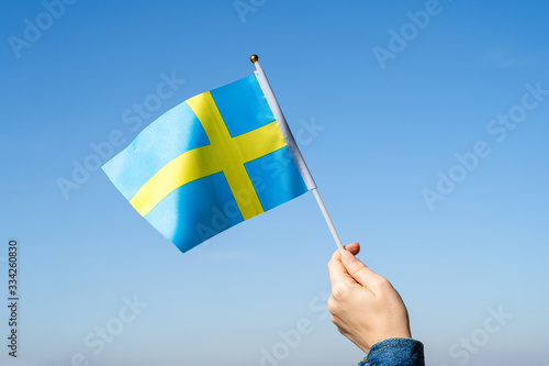 Woman hand with Swedish swaying flag on the blue sky. Sweden. Concept