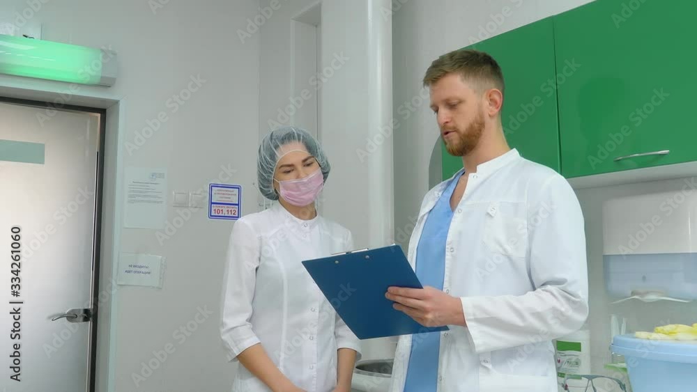 A young doctor in a medical gown discusses the patient's medical record with a beautiful nurse. A young doctor in a medical gown discusses the patient's medical record with a beautiful nurse.