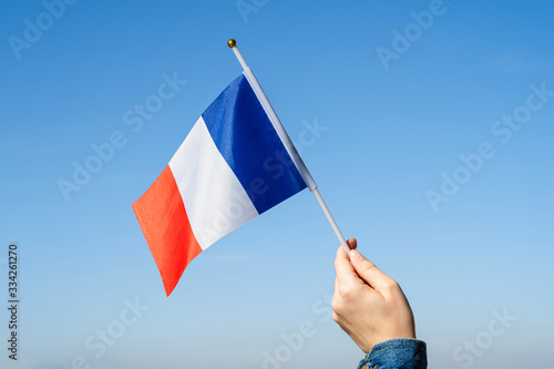 Fotografia Woman hand with French swaying flag on the blue sky