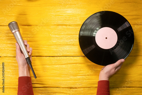 Vinyl record and microphone in female hands on yellow wooden flat lay background with copy space.