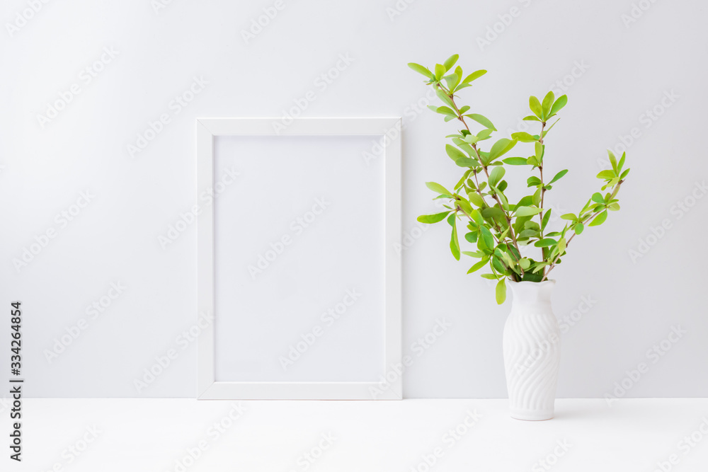 Home interior with decor elements. Mockup with a white frame and branches with green leaves in a vase on a light background Home interior with decor elements. Mockup with a white frame and branches with green leaves in a vase on a light background