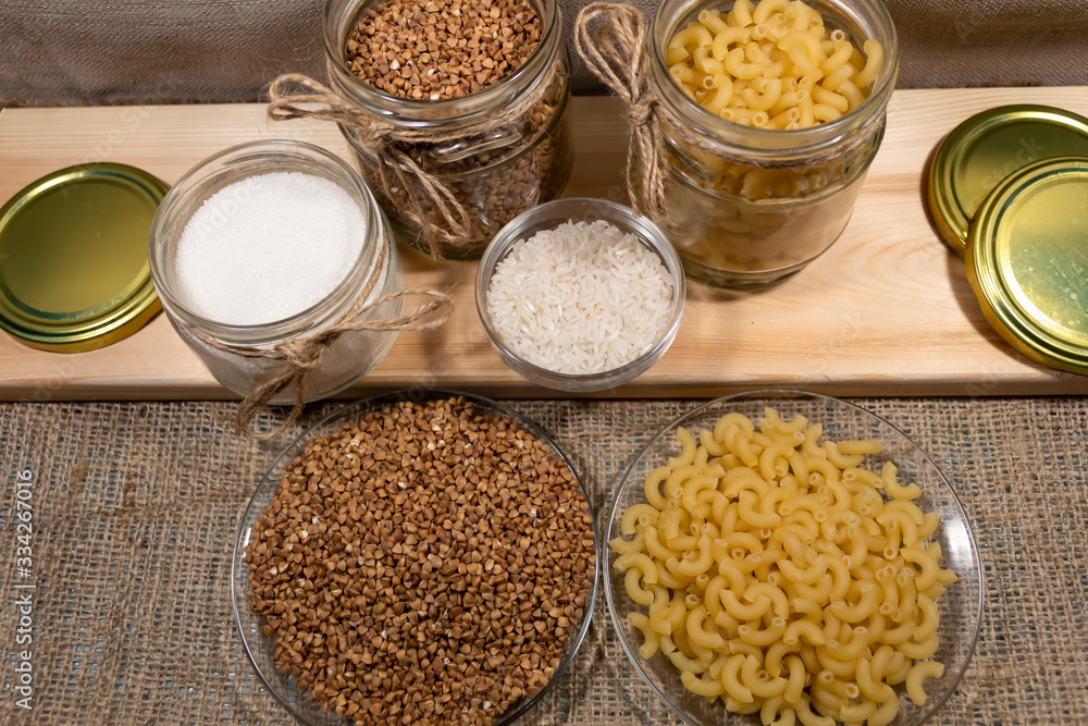 On the board are cans of buckwheat, pasta and sugar. In the bowl lies rice. Buckwheat and pasta also lie on plates. On the board are cans of buckwheat, pasta and sugar. In the bowl lies rice. Buckwheat and pasta also lie on plates.