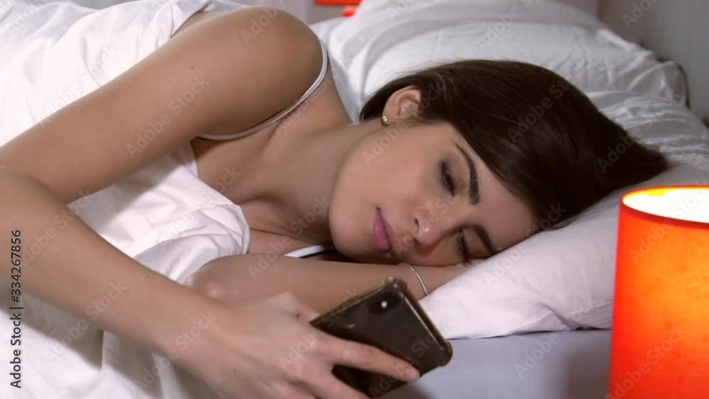 Cute young woman in the morning in bed checking message on phone Cute young woman in the morning in bed checking message on phone