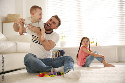 Unhappy little girl feeling jealous while father spending time with her baby brother at home photo