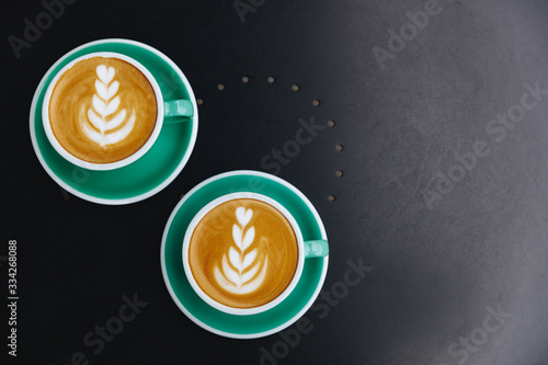 Hot coffee latte art in green ceramic cups with saucers on background of black table. Two persons came to coffee shop to drink tasty aroma cappuccino