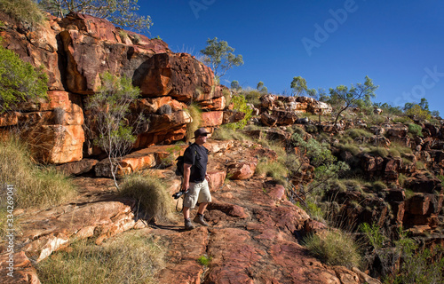 Nature photographer on a hiking trip at the Australian outback at rocky environment between Eucalyptus tree, grass and boulders with blue sky as background