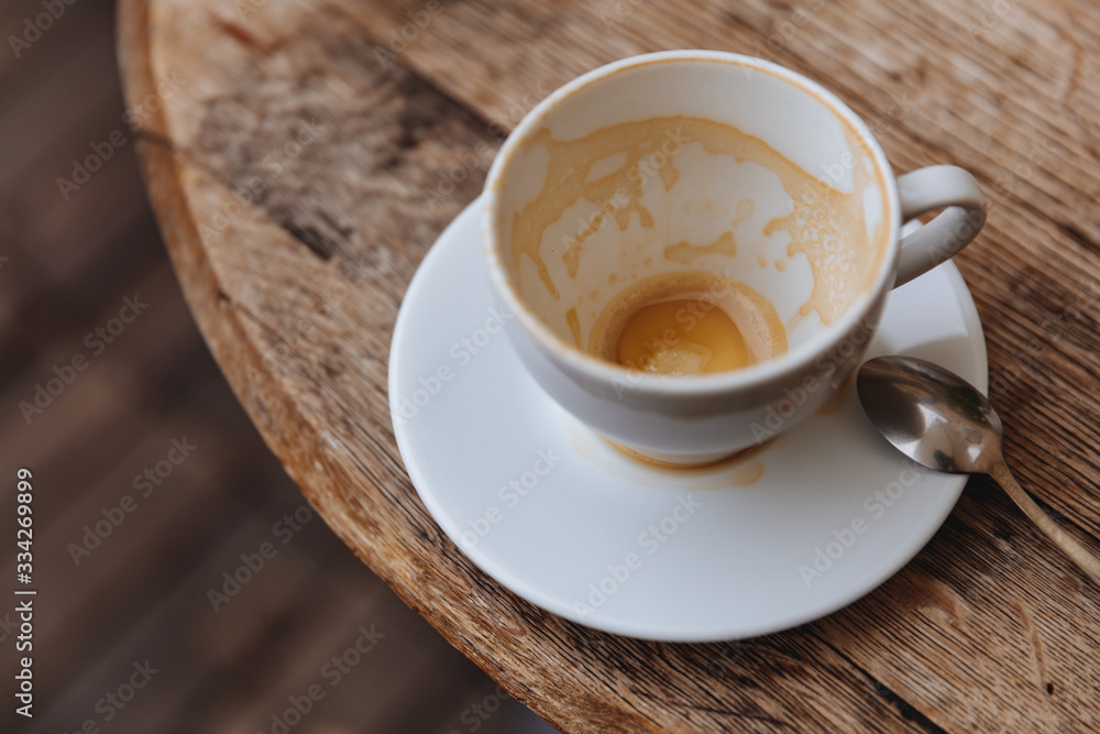 Cappuccino coffee stain in almost empty white cup with milk foam on walls on wooden table with blur background. Frothy coffee in ceramic cup