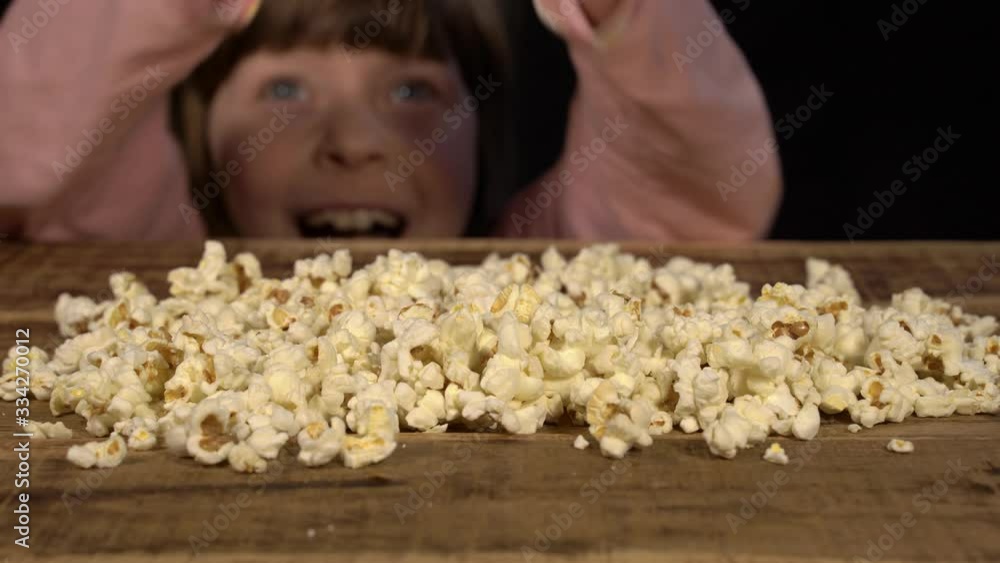 girl secretly takes popcorn from a wooden table. selective focus on popcorn girl secretly takes popcorn from a wooden table. selective focus on popcorn