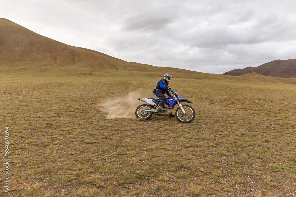 Motorcycle traveler man in helmet riding a motorbike in the steppes of Mongolia.