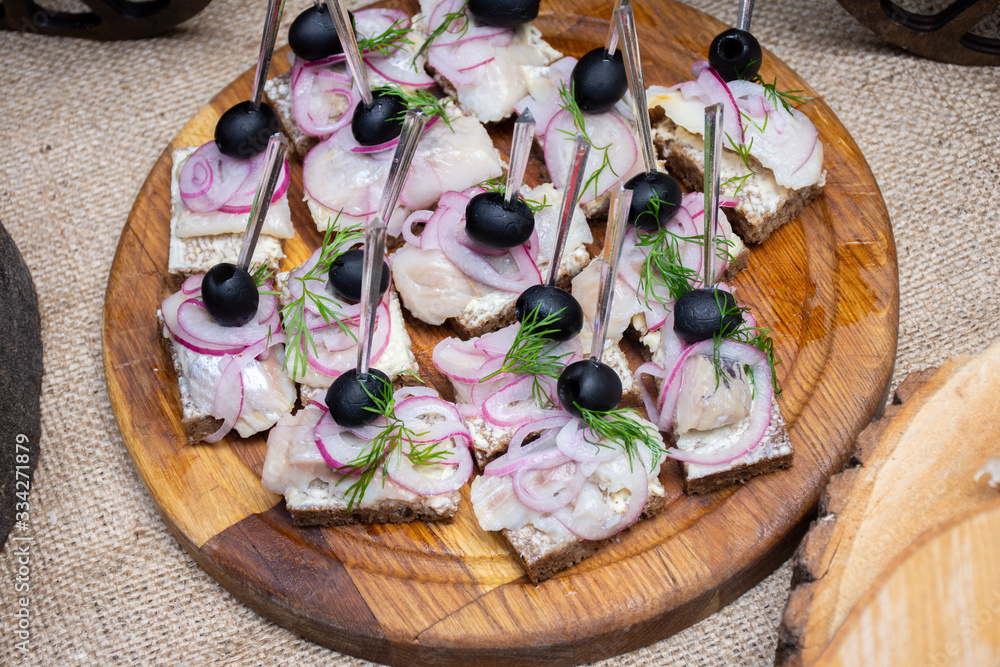 Sandwiches with black bread and herring, onion and olives on a wooden plate