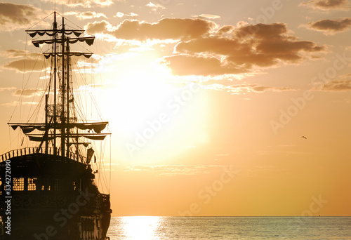 Pirates Ship sails at sea in front of sun horizontal